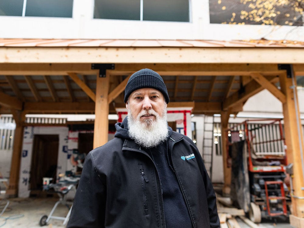  A man with a white beard, black toque and black jacket looks at the camera. 
