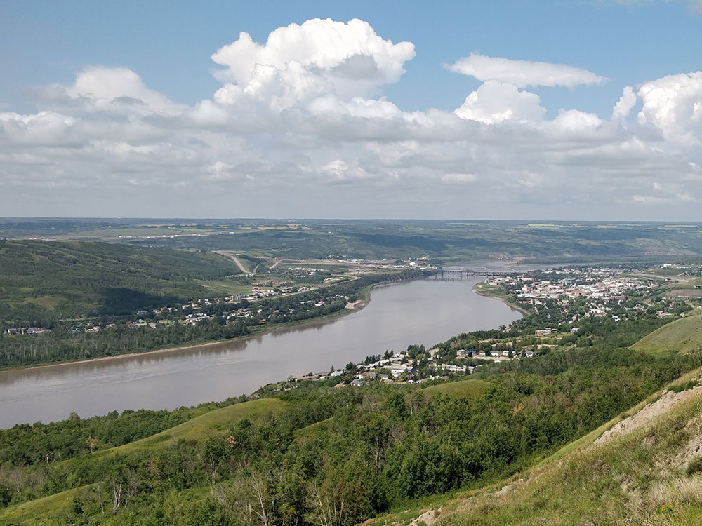 The homes and buildings of a town are strung along both banks of a wide river in an otherwise rural setting.