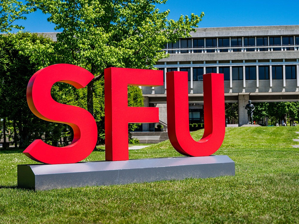 A sign consisting of bright red letters spelling ‘SFU’ stands in front of a two-storey elevated concrete building.