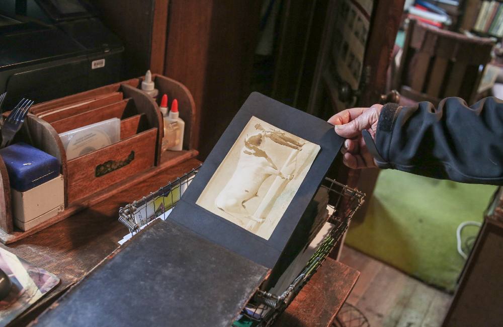 A hand turns to the front page of an old photo album. A sepia-toned photo of a Holstein cow beside a farmer is mounted onto a black page.  The family history, closely intermingled with local history, is not just limited to the house. Steves doesn’t have to wander far to see signs and businesses bearing his family name, which he admits was a bit “embarrassing” growing up.