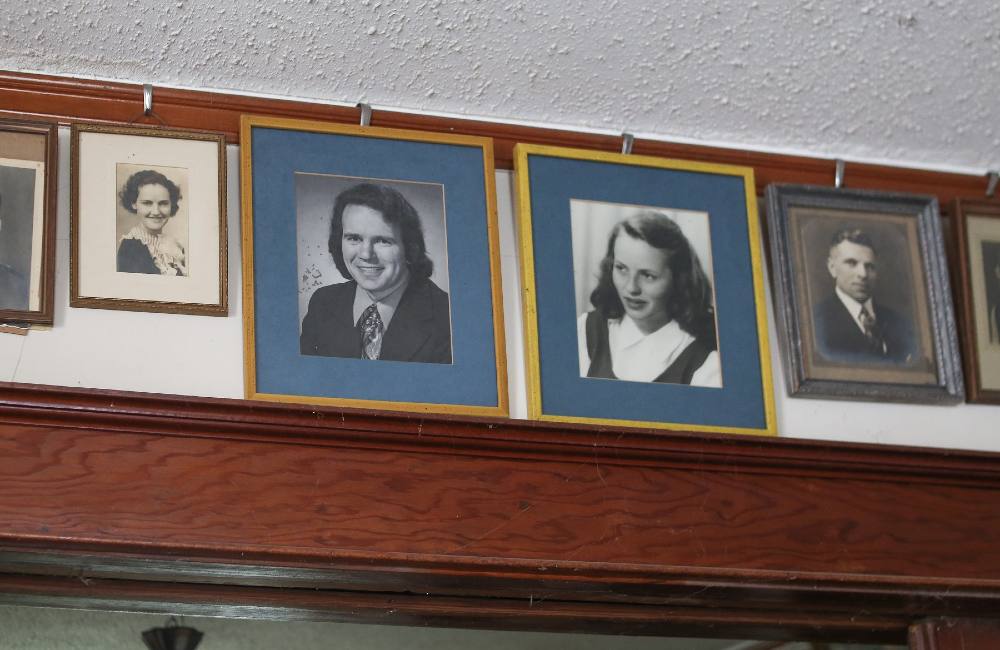 Framed black-and-white portraits of a man with shaggy hair in a suit and tie and woman in a white shirt under a jumper are hanging above a doorway. The photos are mounted on blue mats and in gold frames.