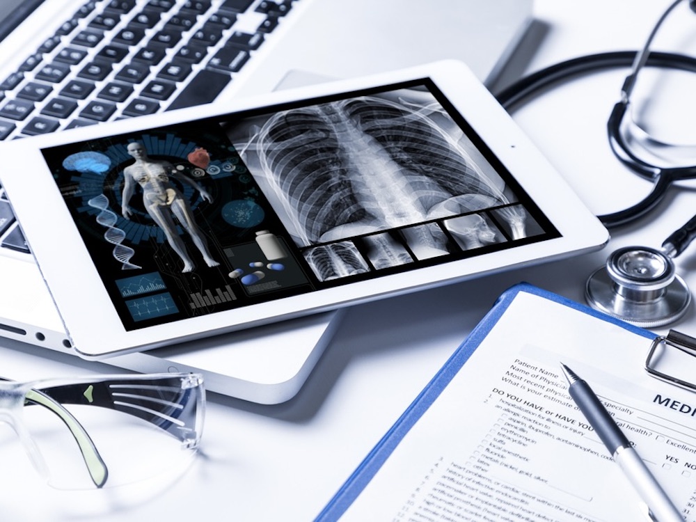 An iPad sits on top of a laptop on a desk. On the screen, an anatomy photo and skeletal scans.