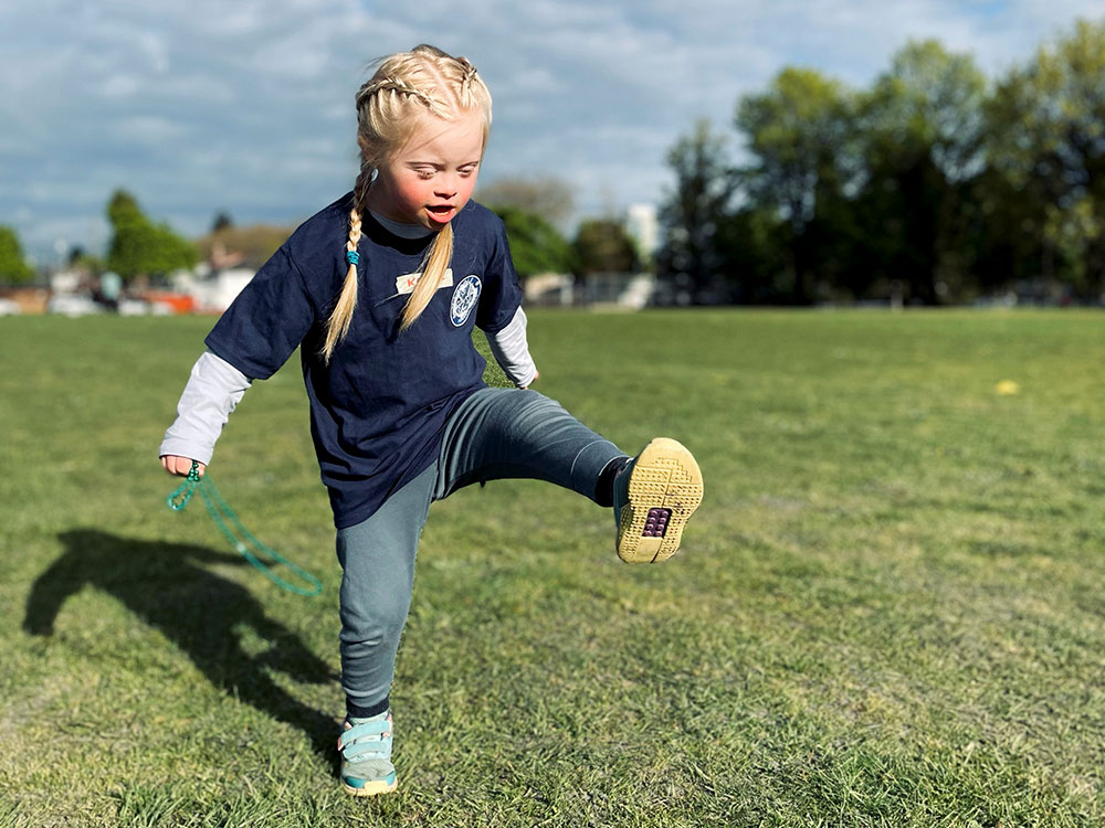 A blonde-haired girl kicking her leg up in a field.