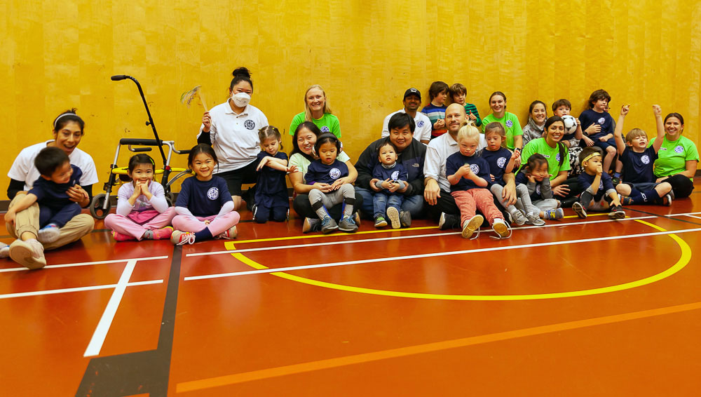 Kids and parents sit in rows on a gymnasium floor.