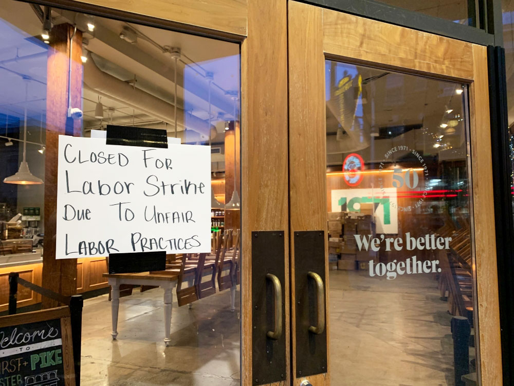 A photo shows the closed glass doors of a coffee shop and a white hand-lettered sign saying ‘Closed for Labor Strike Due To Unfair Labor Practices.’ 