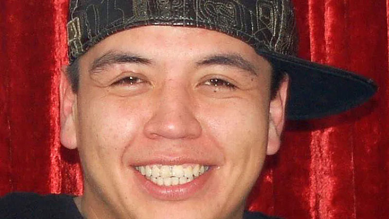 A photo shows a young man smiling at the camera, wearing a T-shirt and sideways cap.