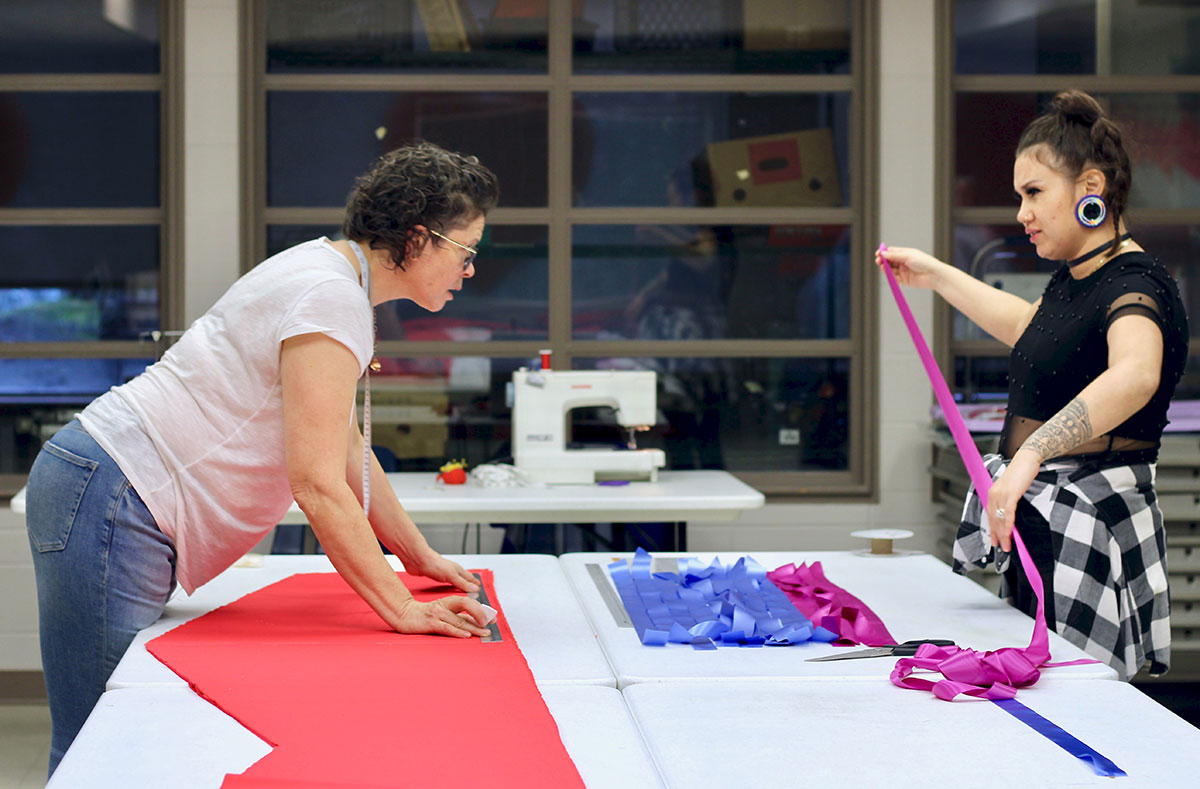 Two women lean across a table swathed in red fabric.