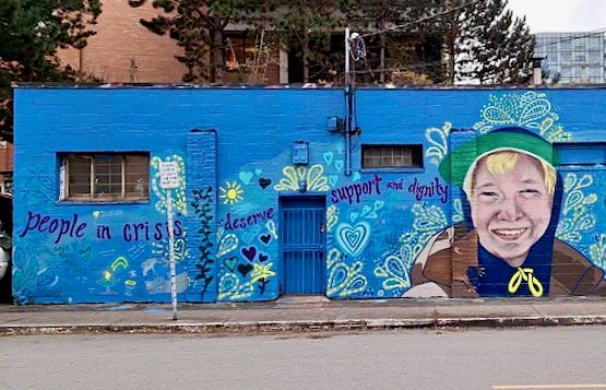 A mural of Dani Cooper is painted on a blue background. Text on the mural reads, “People in crisis deserve support and dignity.”