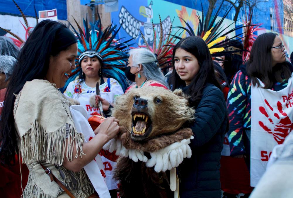 A woman smiles at a grizzly bear had while another person holds it and three women talk in the background.