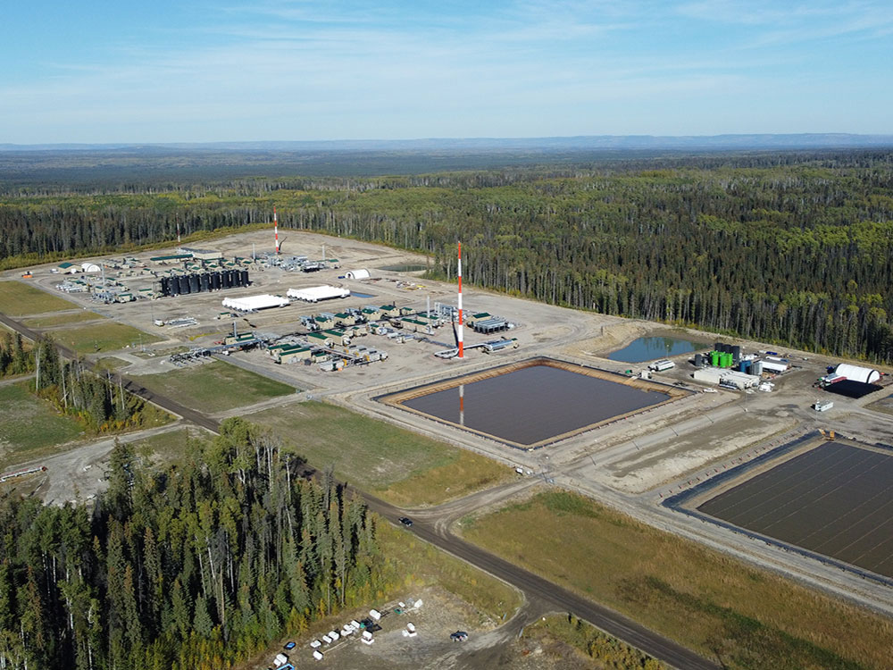 An industrial site that includes mechanical equipment and water holding facilities. The site is surrounded by a flat, treed landscape.