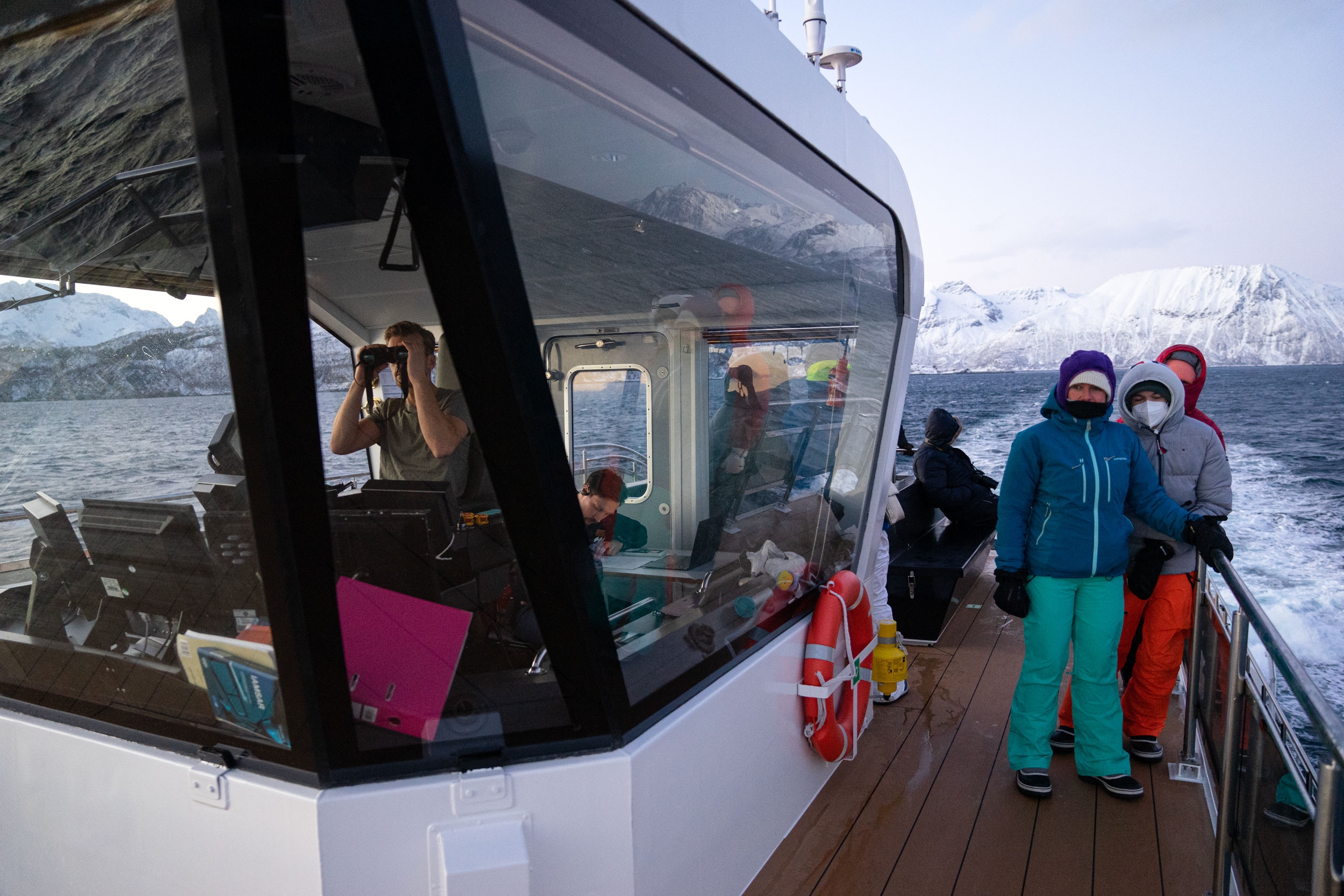 People in snowsuits stand on the deck of a boat that is moving through cold, icy ocean waters.