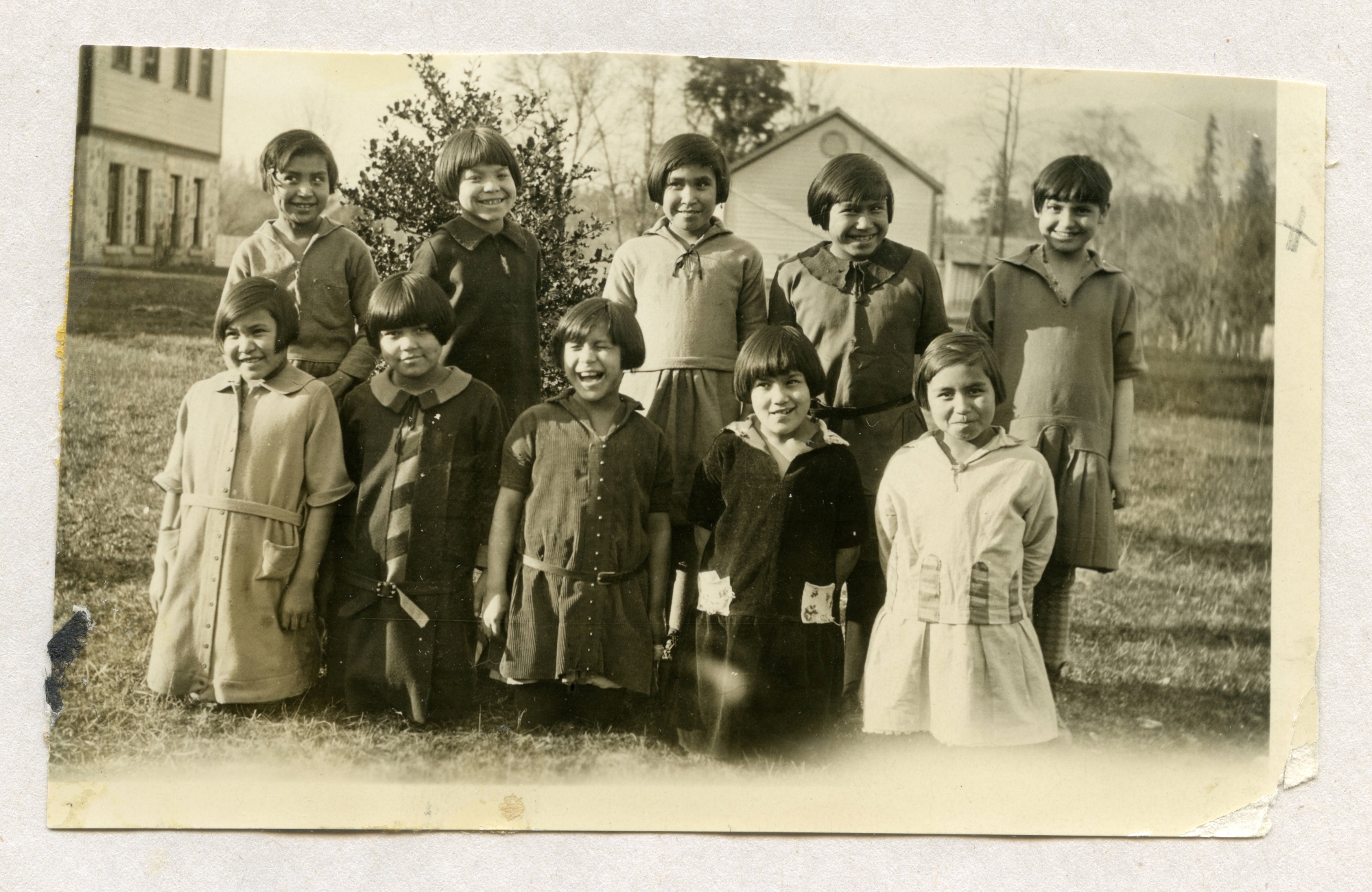 Ten girls, about nine years old, smile at the camera in a black-and-white photo. Five are kneeling and another five stand behind them. They all have similar basic haircuts.