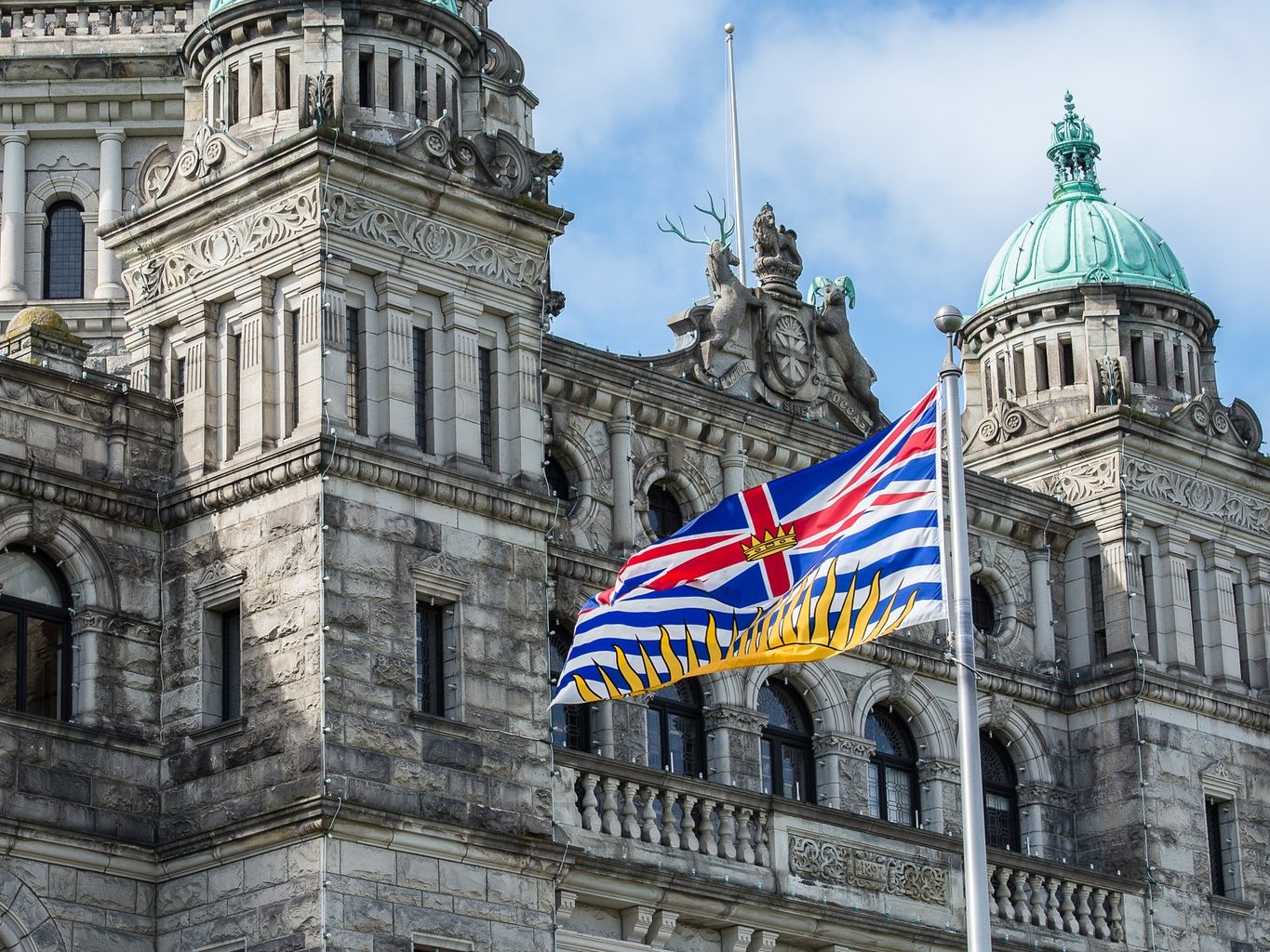 A BC flag flies in front of the stone legislature building.