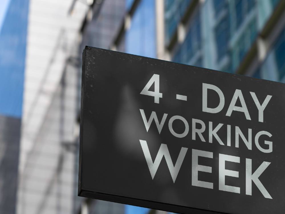 A slate grey sign attached to an office building says “4-day working week.”