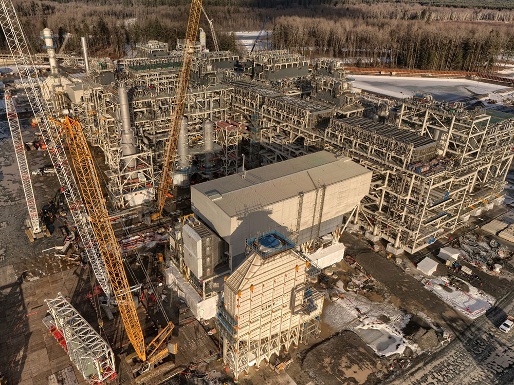 An aerial shot shows a building site with large open-framed metal structures and construction cranes.