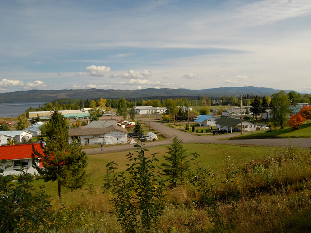 Streets and homes in a small community next to a lake. Low, hilly mountains are visible in the background.