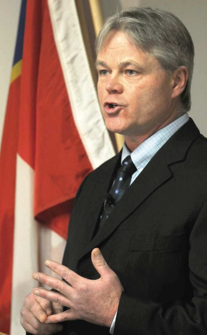 A man in a suit stands, giving a speech.