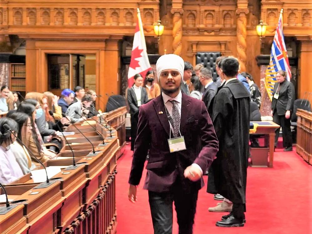 A young man wearing a suit and Sikh turban stands in a legislative chambers.