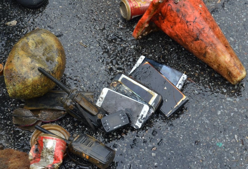 Dirty, water-logged cellphones and walkie talkies are on the ground between a couple orange traffic cones.