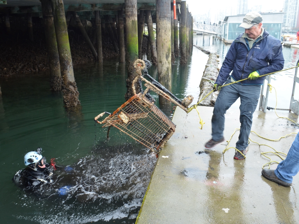City workers help pull a barnacle-encrusted shopping cart from the water. Henry Wang, wearing a Go-Pro, is in the water. He’s wearing a drysuit.