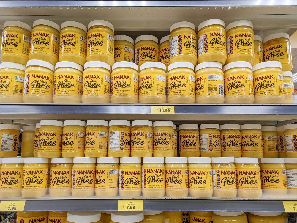 Shelves of Nanak-brand ghee in small and large sizes. The ghee inside is a bright yellow.