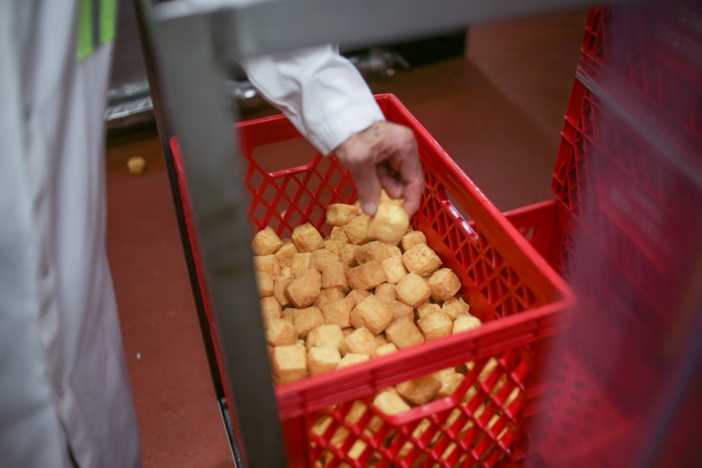 A hand pinches a tofu puff out of a red carton.