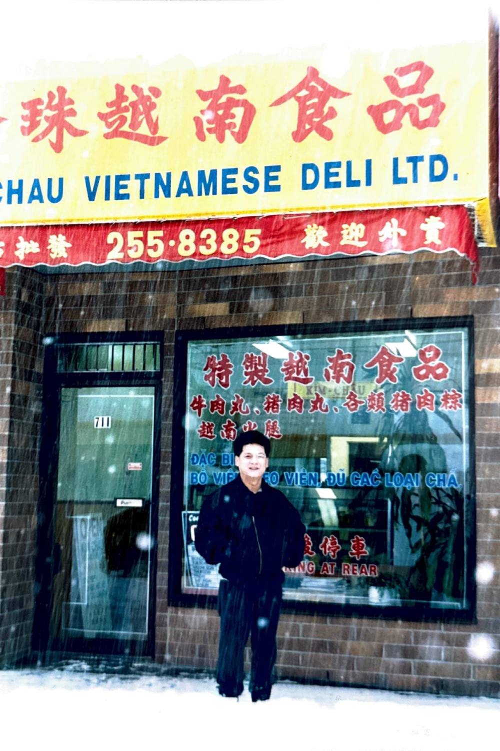 A photo from the late-1980s showing a man smiling in front of a Vietnamese deli. It is a snowy day.