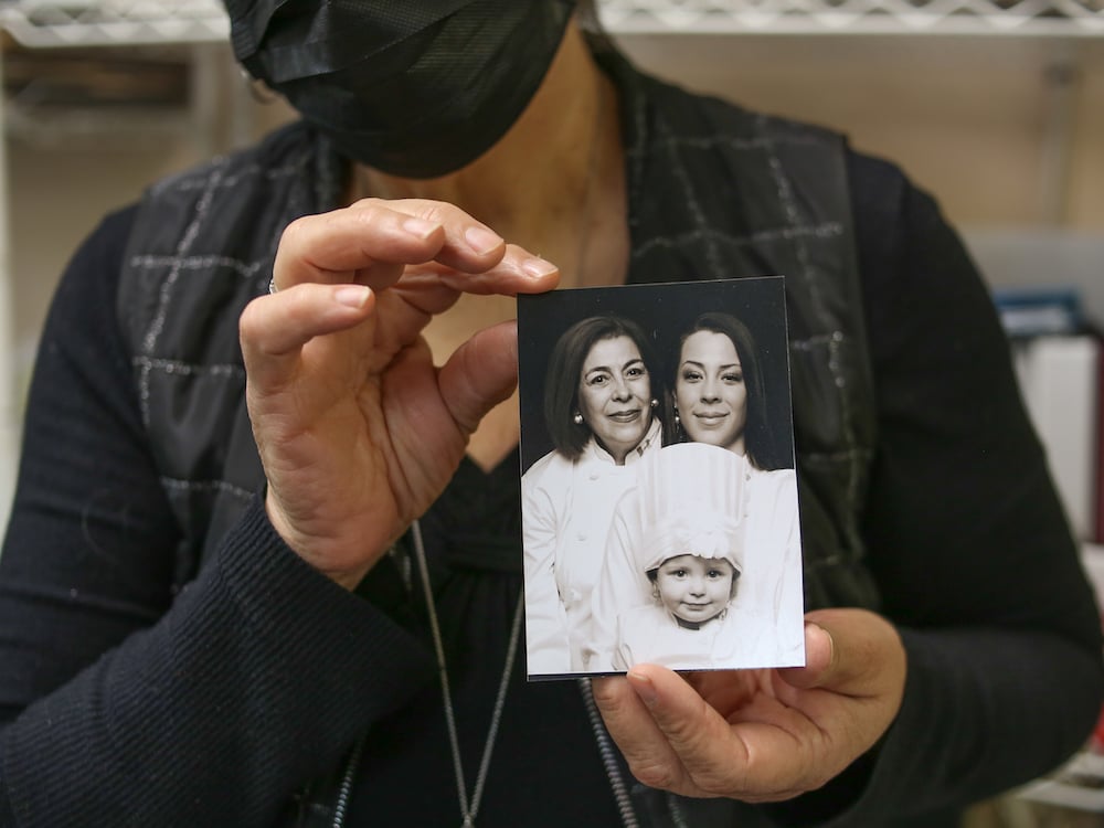 A pair of aging hands holds a black-and-white photograph of a grandmother, mother and an adorable two-year-old granddaughter in a chef’s hat.