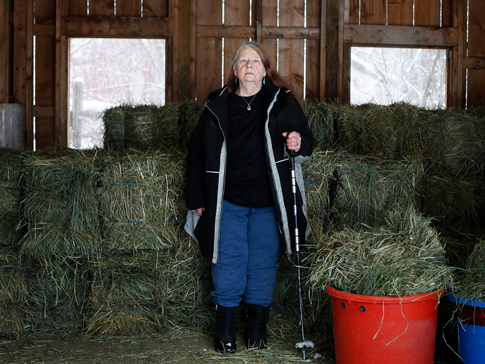A woman standing in a barn in front of stacks of hay.