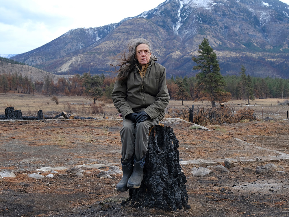 A woman sitting on a burned tree stump.