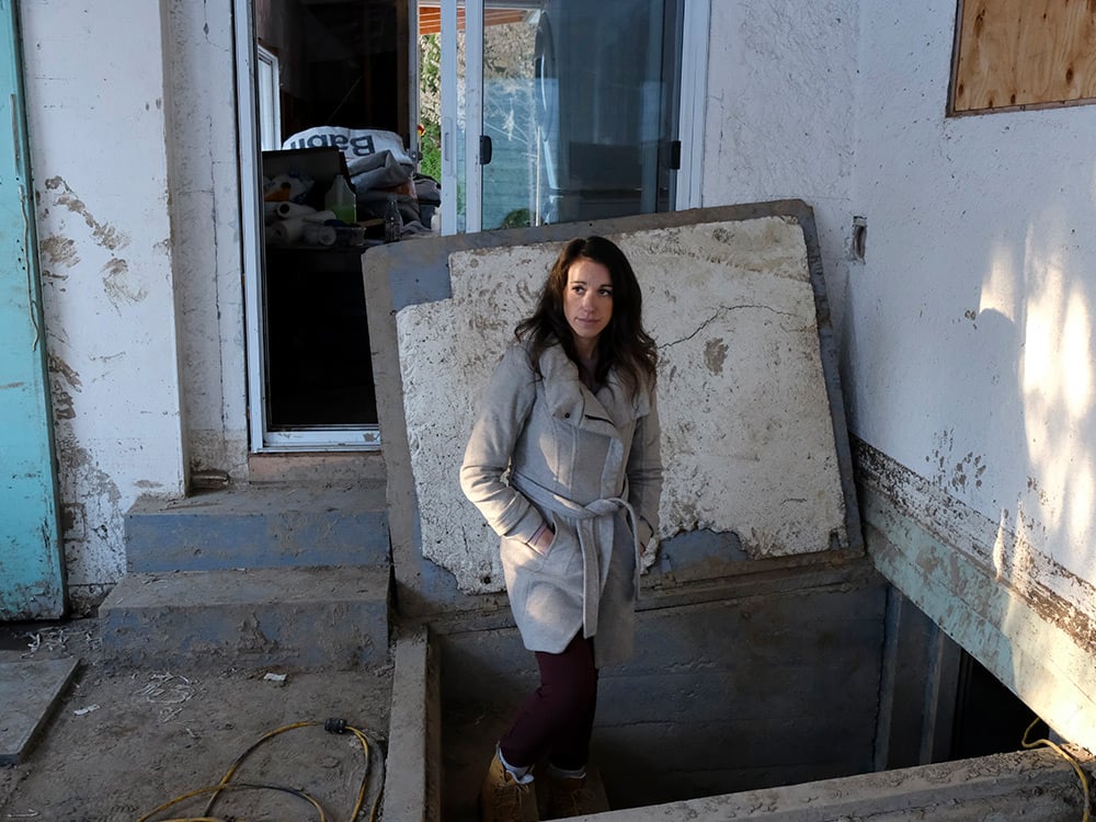 A woman on the steps leading to a basement of a damaged house.