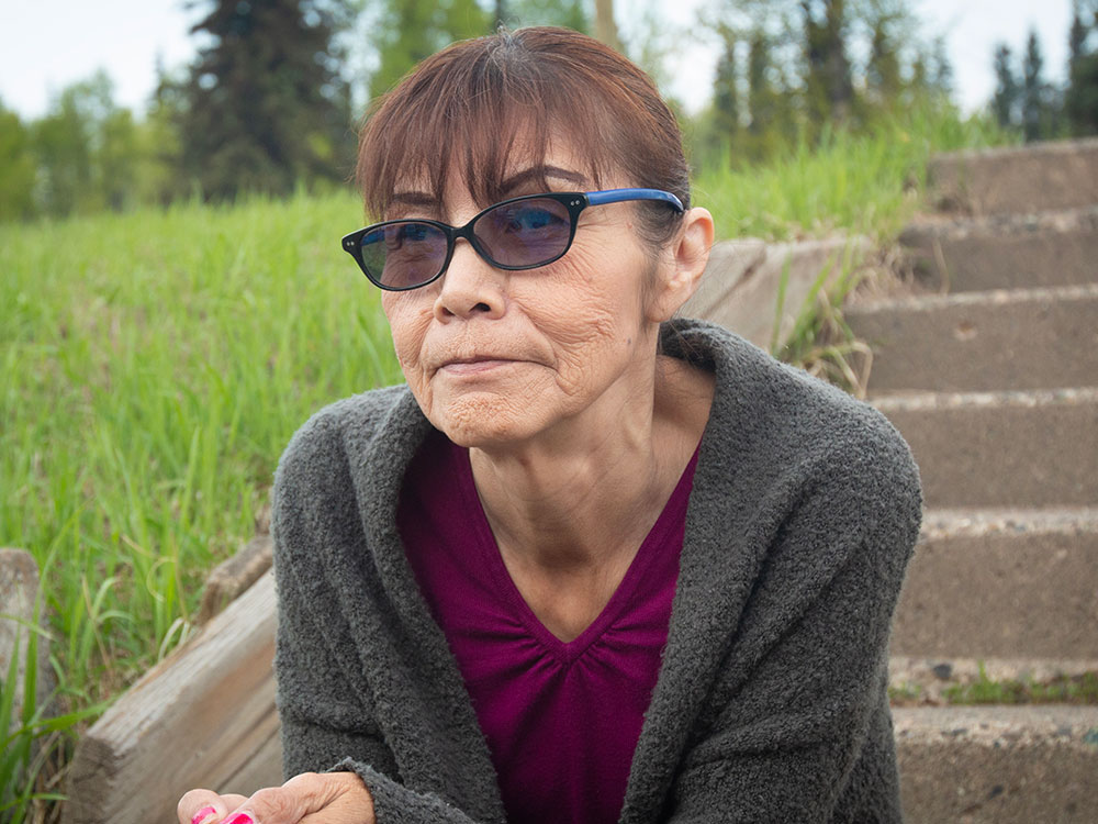 A woman with brown hair sits on concrete steps, looking just off-camera. Her expression is sombre but she has a sparkle in her eye.