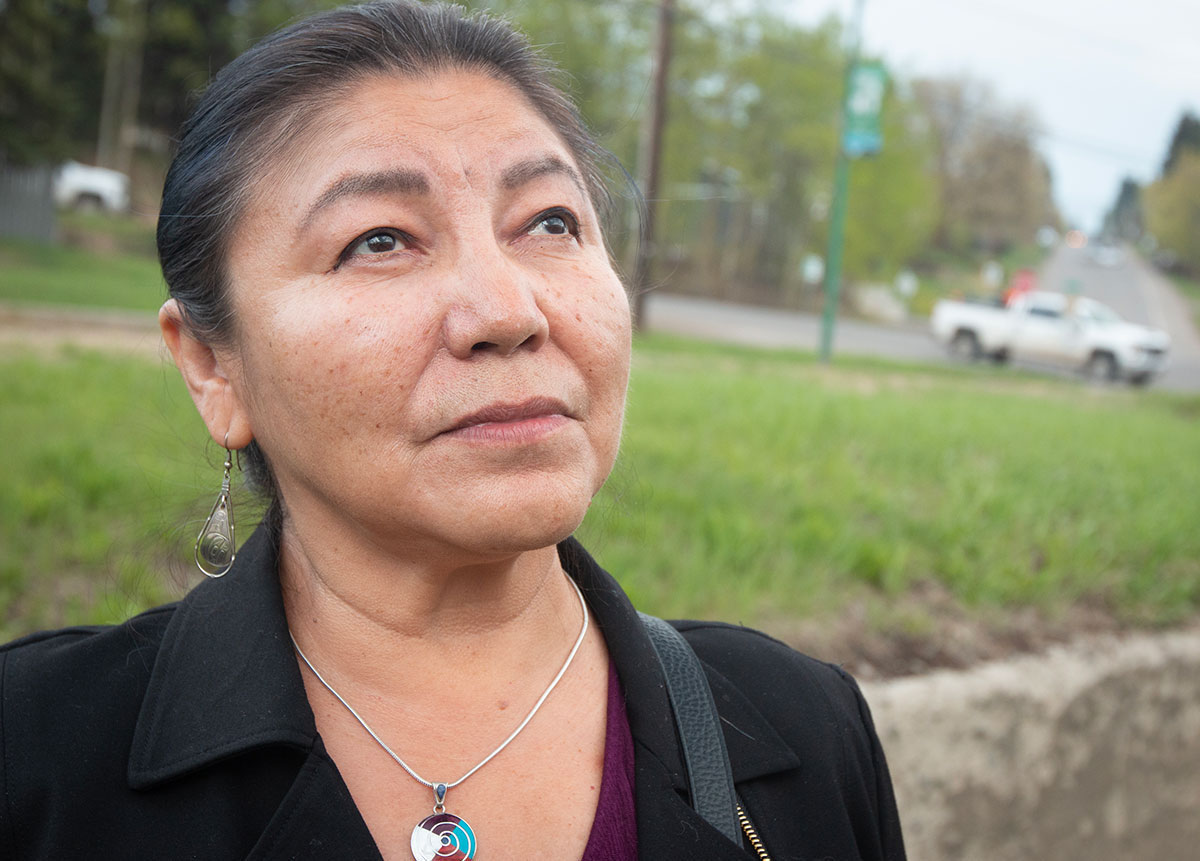 A closeup photo of a woman with her dark hair pulled back off her face. She looks up towards the sky.