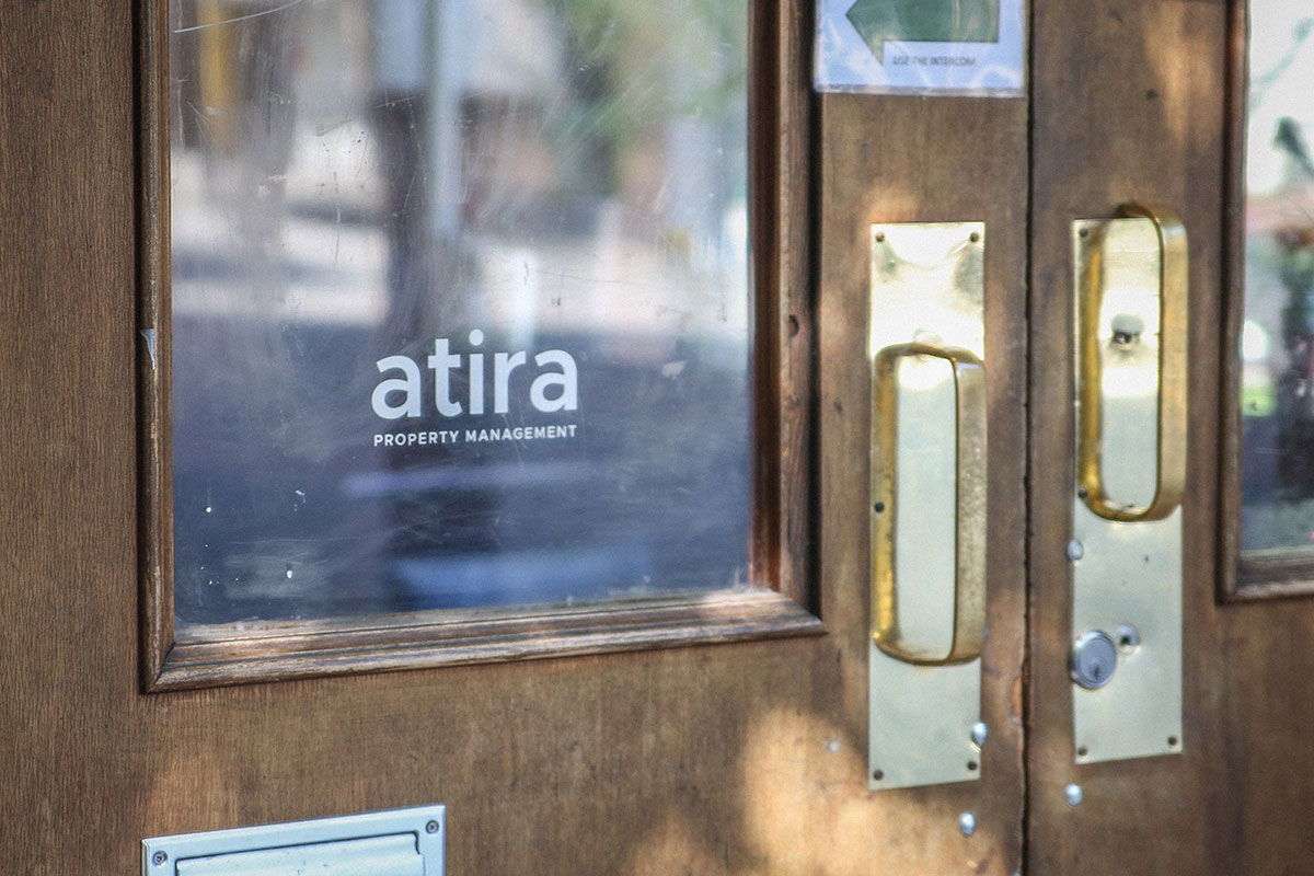 The front door of 303 Columbia features an Atira property management logo on the glass. The door includes wood panelling and gold handles.