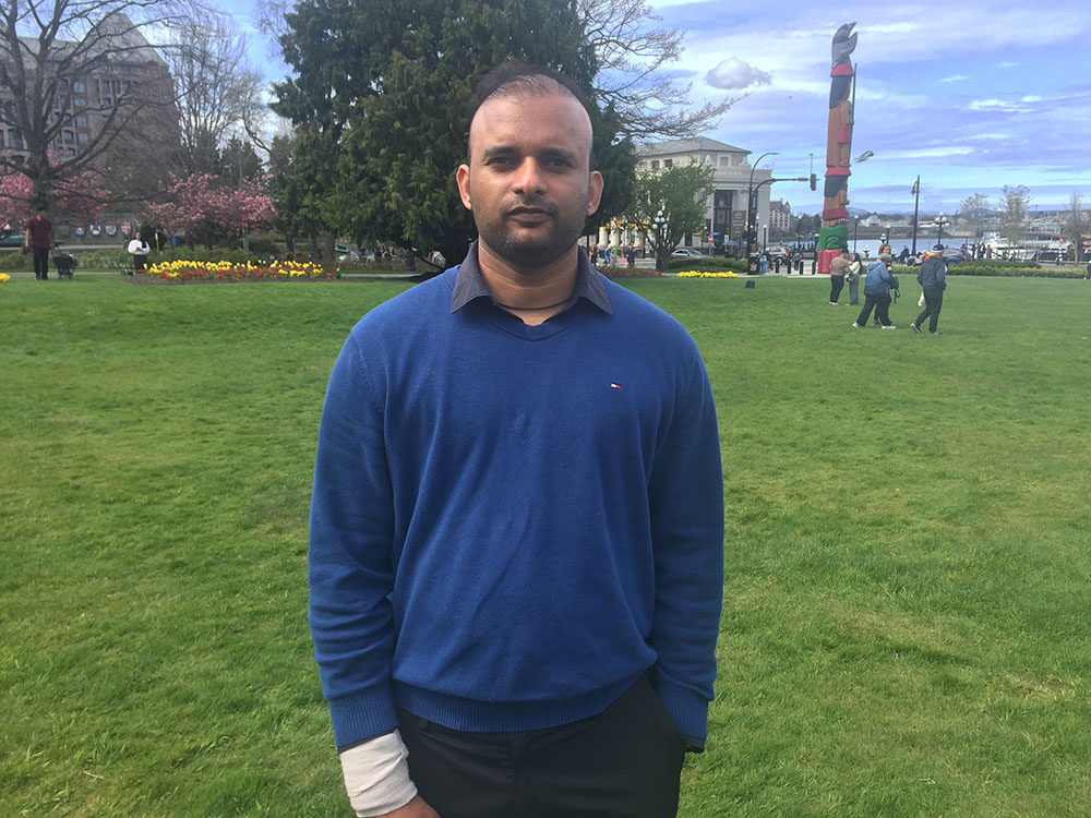 Aman Sood looks at the camera, wearing a blue sweater and dark pants.