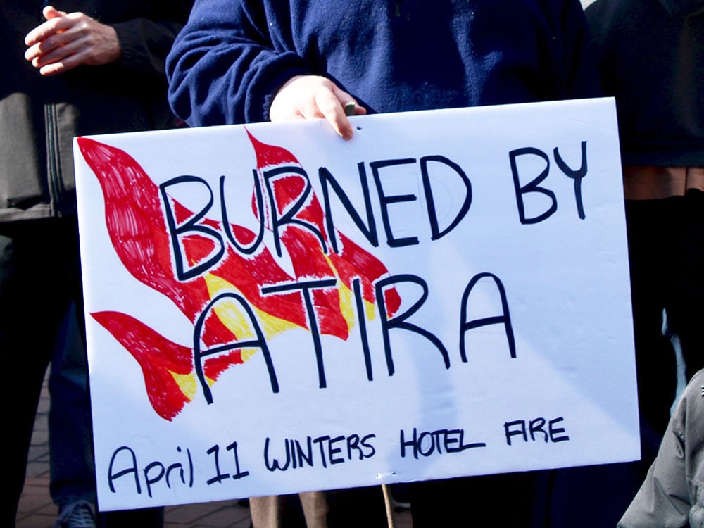 A white sign says “Burned by Atira” with flames in the background.