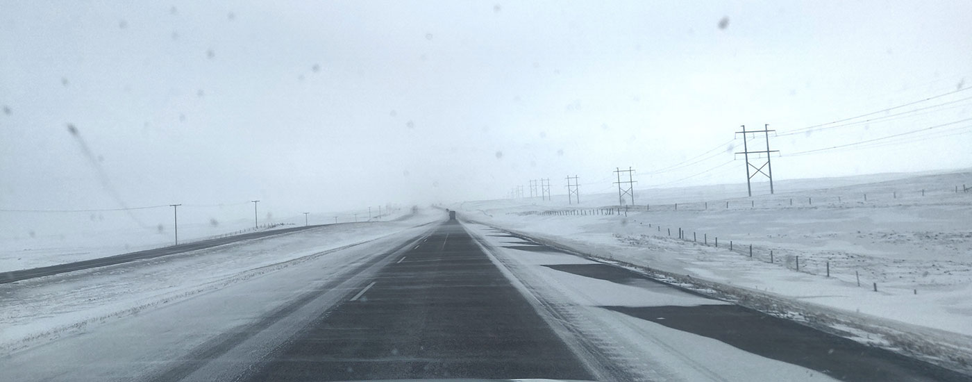 The Trans Canada highway in the snowy prairies: wind blows snow across the road. There are only two cars visible.