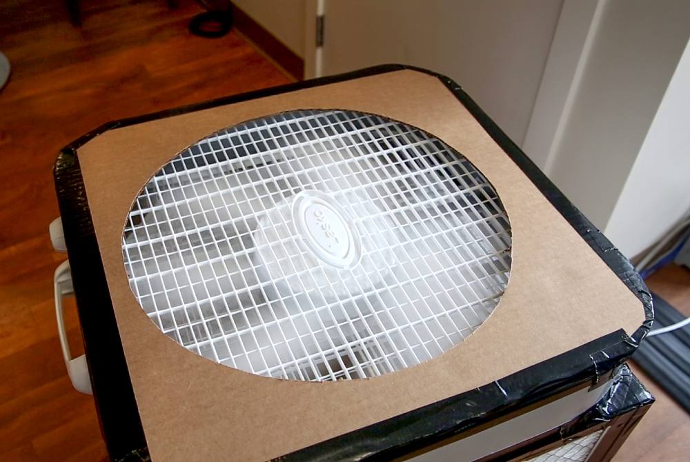 The top of a Corsi-Rosenthal Box features a large white fan blowing air through a circular brown cardboard ‘shroud.’