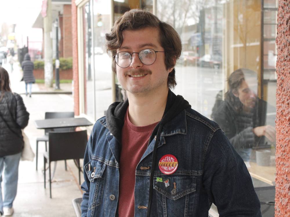 Eddy Pedreira, wearing a jean jacket and glasses, smiles at the camera outside a Vacouver coffee shop.