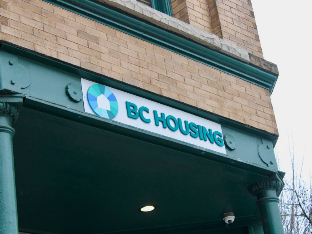 A BC Housing sign on an old brick building.