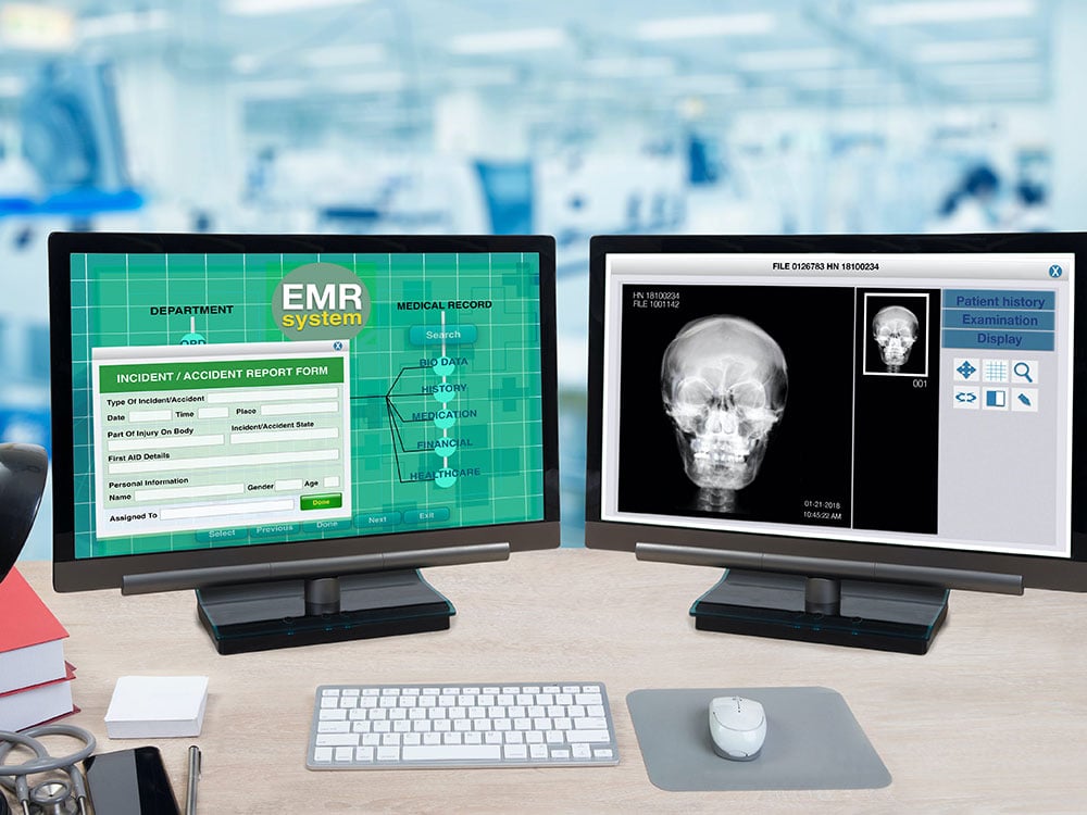 A desk with two computer monitors, one with an X-ray and another showing an accident report.