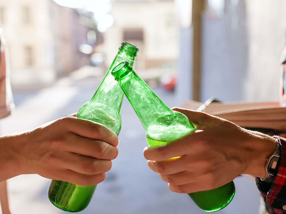Two hands holding green beer bottles tap the necks together.