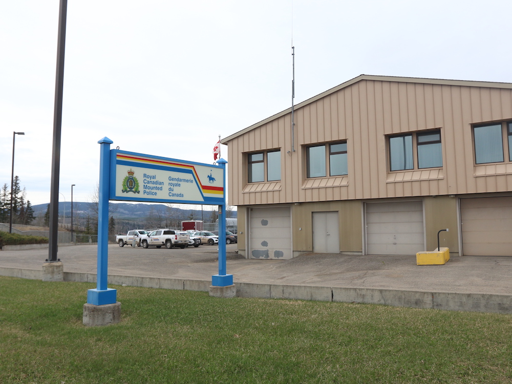 A tan, two-storey building with vehicle bays. There are RCMP-branded vehicles in the parking lot, and a sign that reads, “Royal Canadian Mounted Police” in English and French.