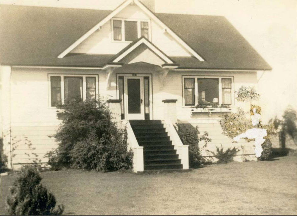 A two-storey single family detached home with white walls, a yard and two large sets of windows on either side of the front patio. 