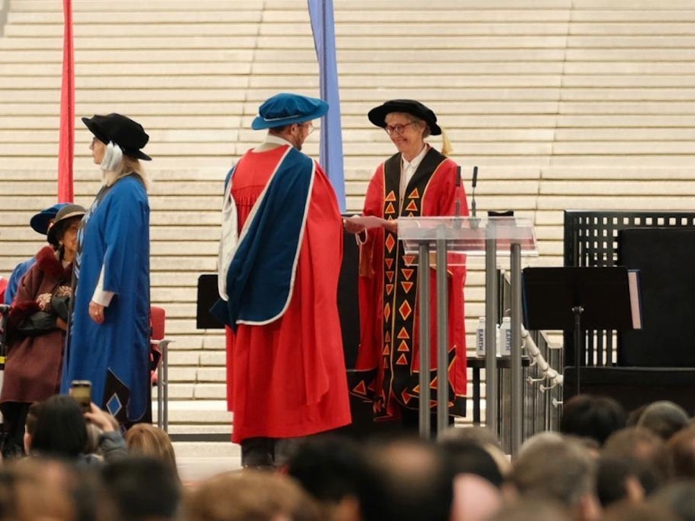 A man in a red robe, blue hat and blue sash hands a strike notice paper to a woman wearing a red hat and a red robe with black triangles.