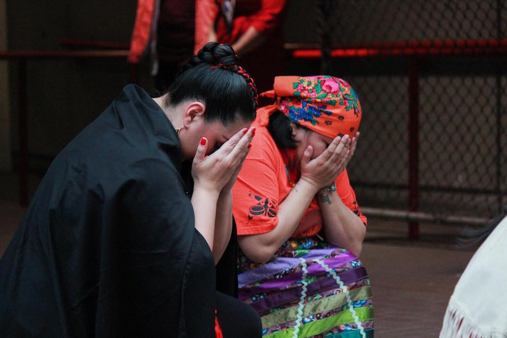Two people kneel with their heads buried in the hands on a stage.