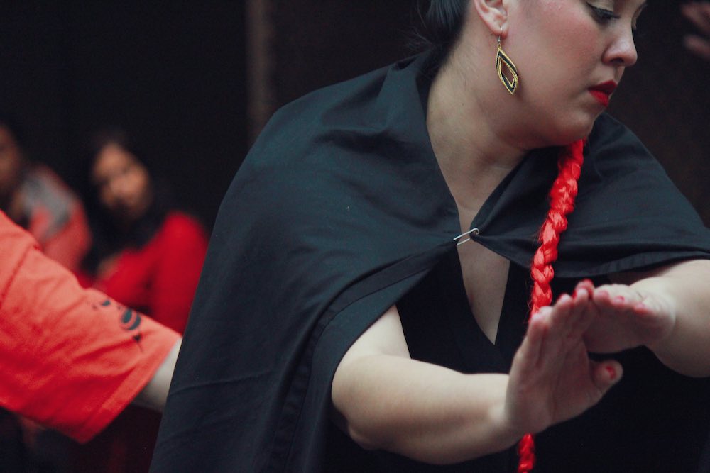 A closeup of dancer Jacqueline Michell in performance, wearing a black cape with a long red braid.