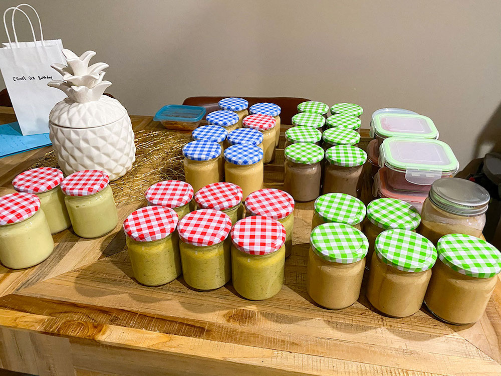 About 35 jars and other containers full of pureed food sit on a table.