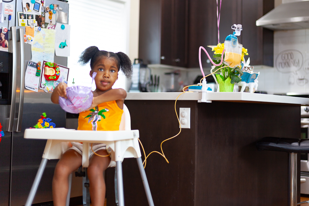 A young girl sits in a high chair and consumes a meal via g-tube.