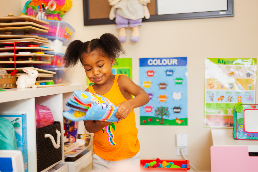 A kid wearing an orange tank top with sequins plays with a fabric book.